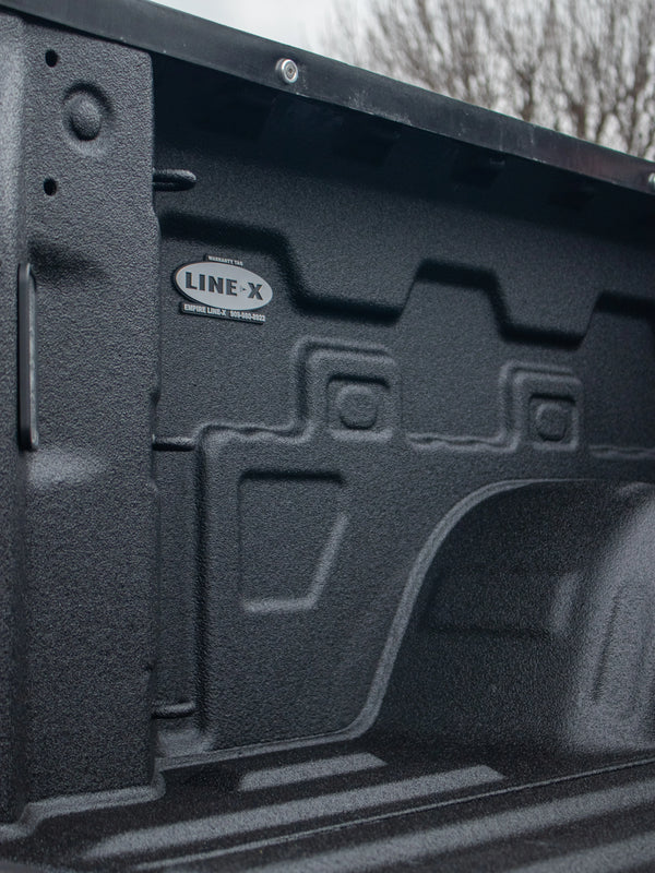 Close-up of a pickup truck bed interior protected with a textured black LINE-X spray-on bedliner.