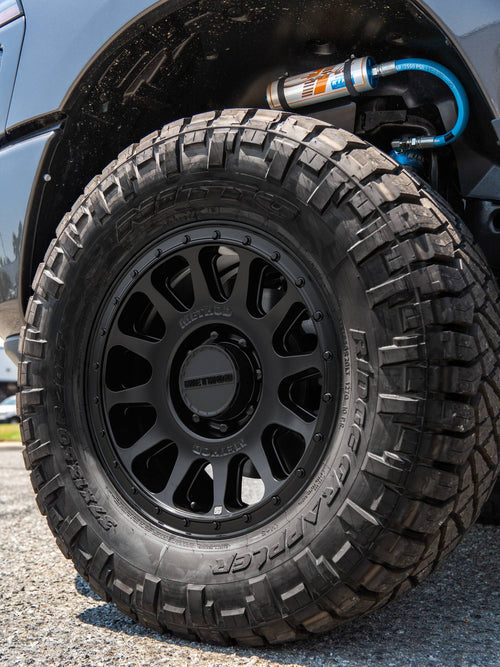 Close-up of a black Method wheel with a Nitto Ridge Grappler tire and a King shock with blue lines