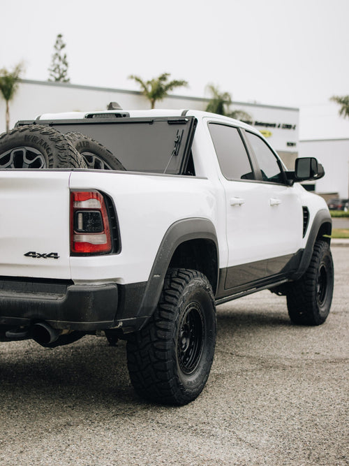 Rear three-quarter view of a white RAM 1500 TRX with a BAKFlip tonneau cover and black wheels