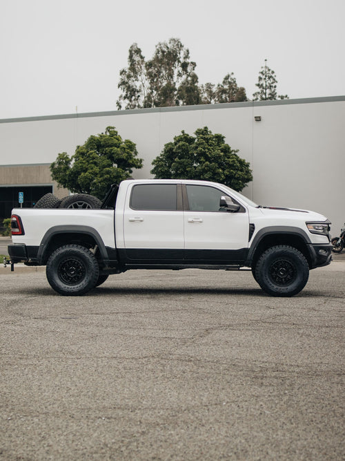 Full side view of a white RAM 1500 TRX with custom black wheels and tires parked by a building
