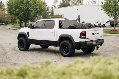 Rear three-quarter view of a white RAM 1500 TRX with Fuel wheels and a BAKFlip cover folded open over the bed