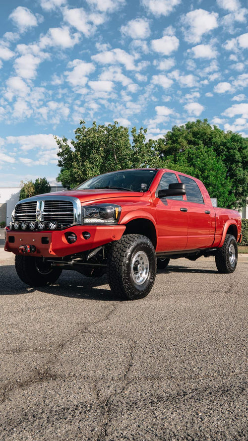 Front three-quarter view of a lifted red Dodge Ram HD under a blue sky with clouds