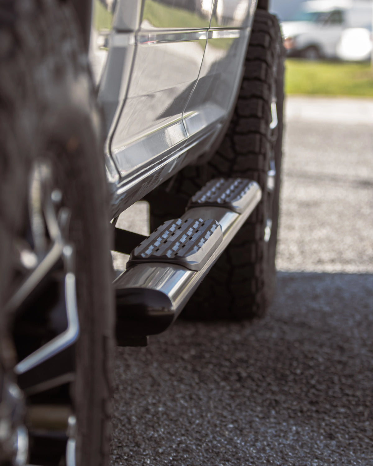 Close-up of a chrome truck running board with textured black step pads beside an off-road tire.