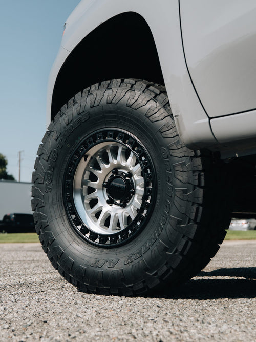 Front wheel of a white truck with a silver KMC wheel and Toyo Open Country tire, low angle